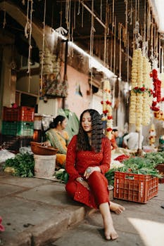 Woman sitting at a colorful market, surrounded by flowers and produce.