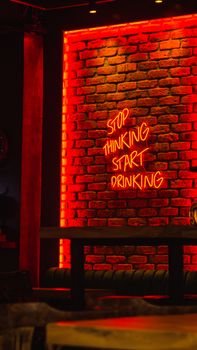 Vibrant neon sign reading 'Stop Thinking, Start Drinking' on a brick wall in a Turkish bar.