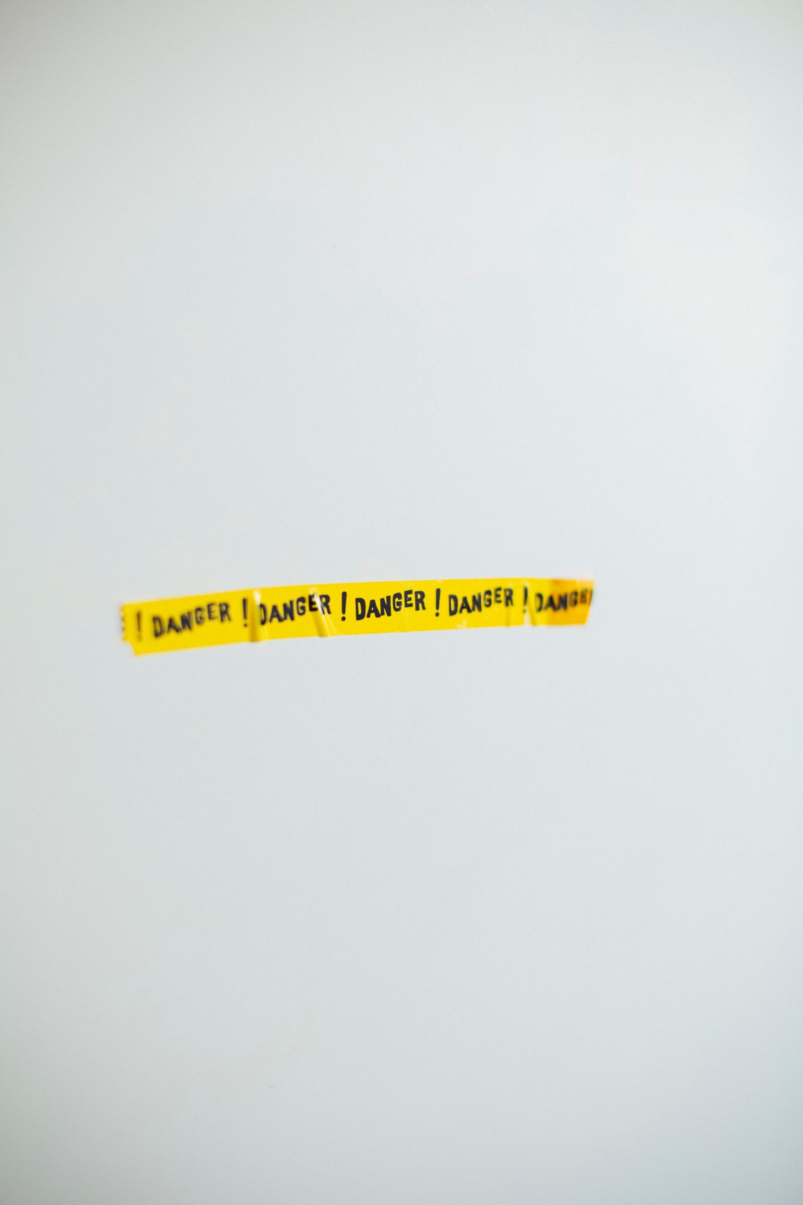 A short strip of yellow tape printed DANGER across a wide, plain gray wall