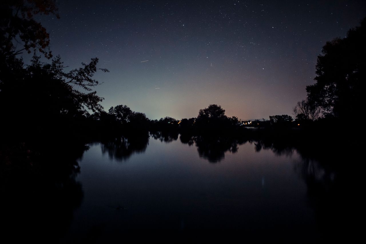 peaceful lakeside view with starry night sky reflecting on calm waters