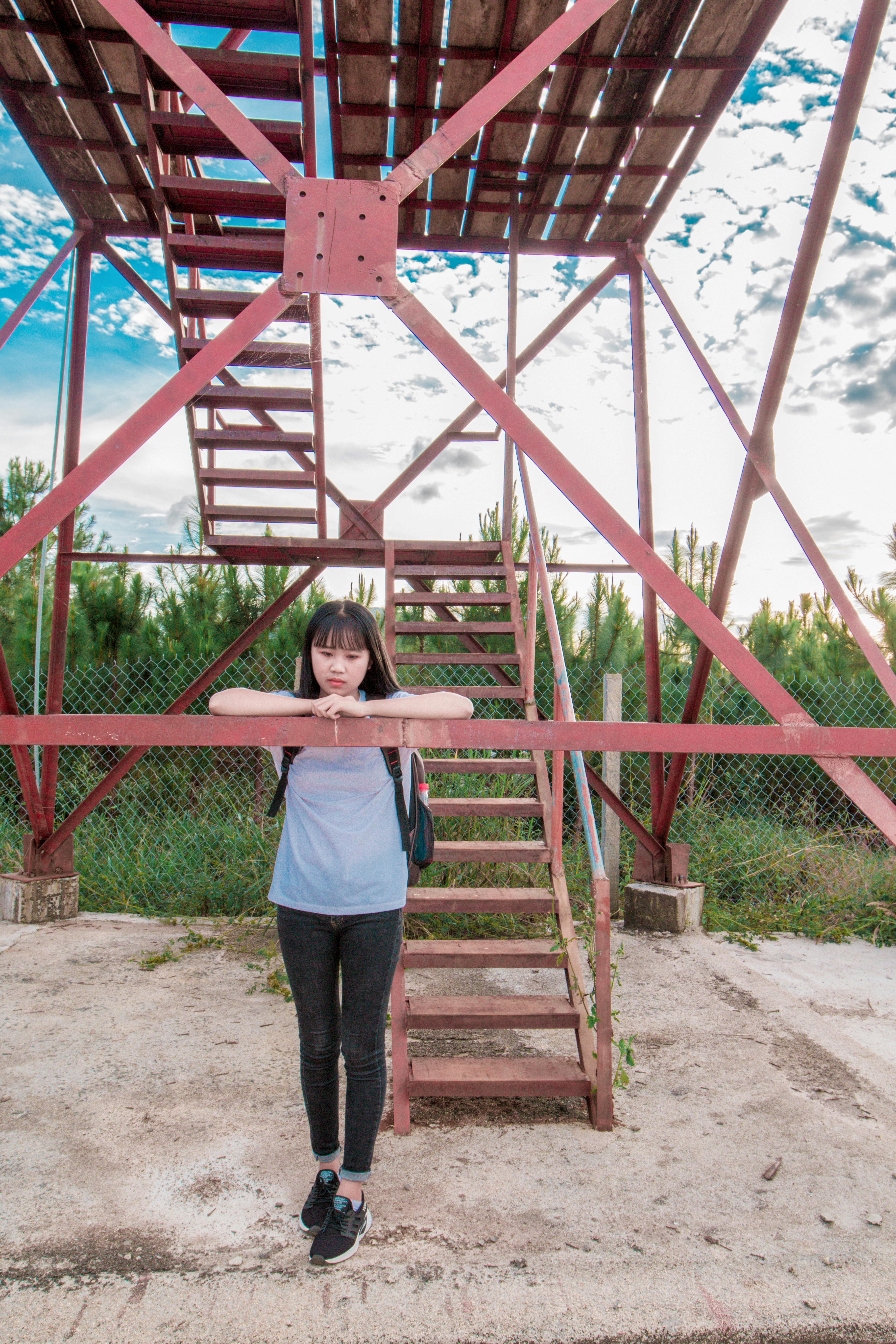 Woman Leaning on Red Metal Tower