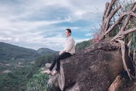 一名男子坐在倒下的树上，俯瞰着映照自然风光的山景