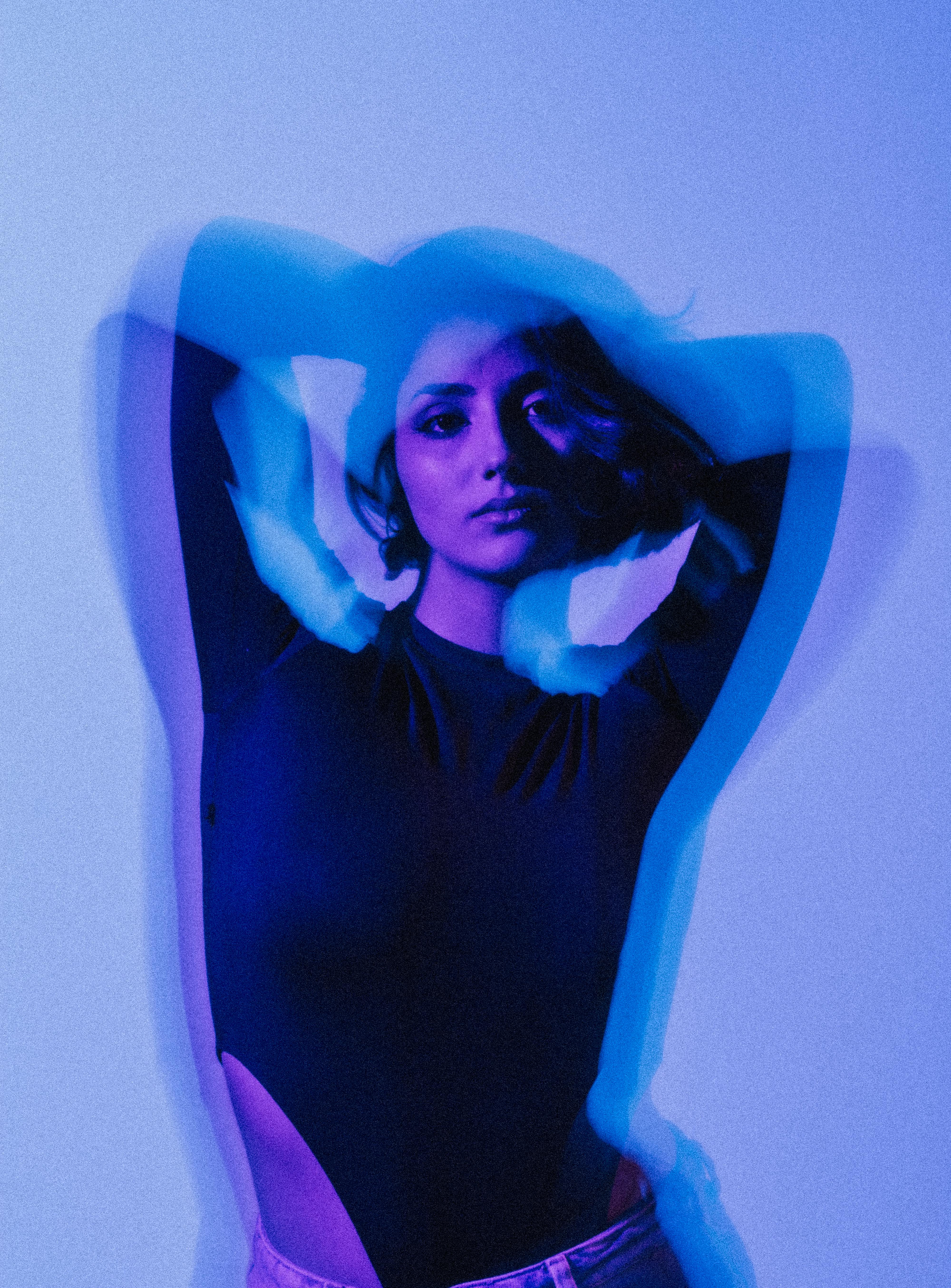 Artistic portrait of a woman using a double exposure effect with vibrant blue and purple lighting.