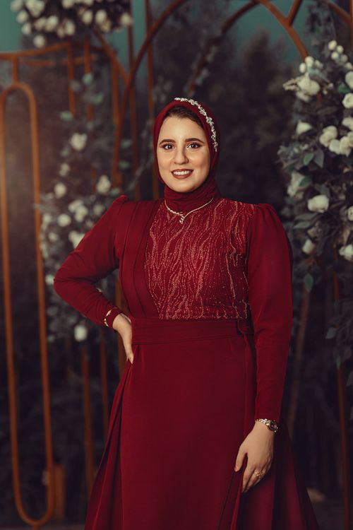 Free Portrait of a smiling woman in a stunning red dress, posing indoors with floral decor. Stock Photo