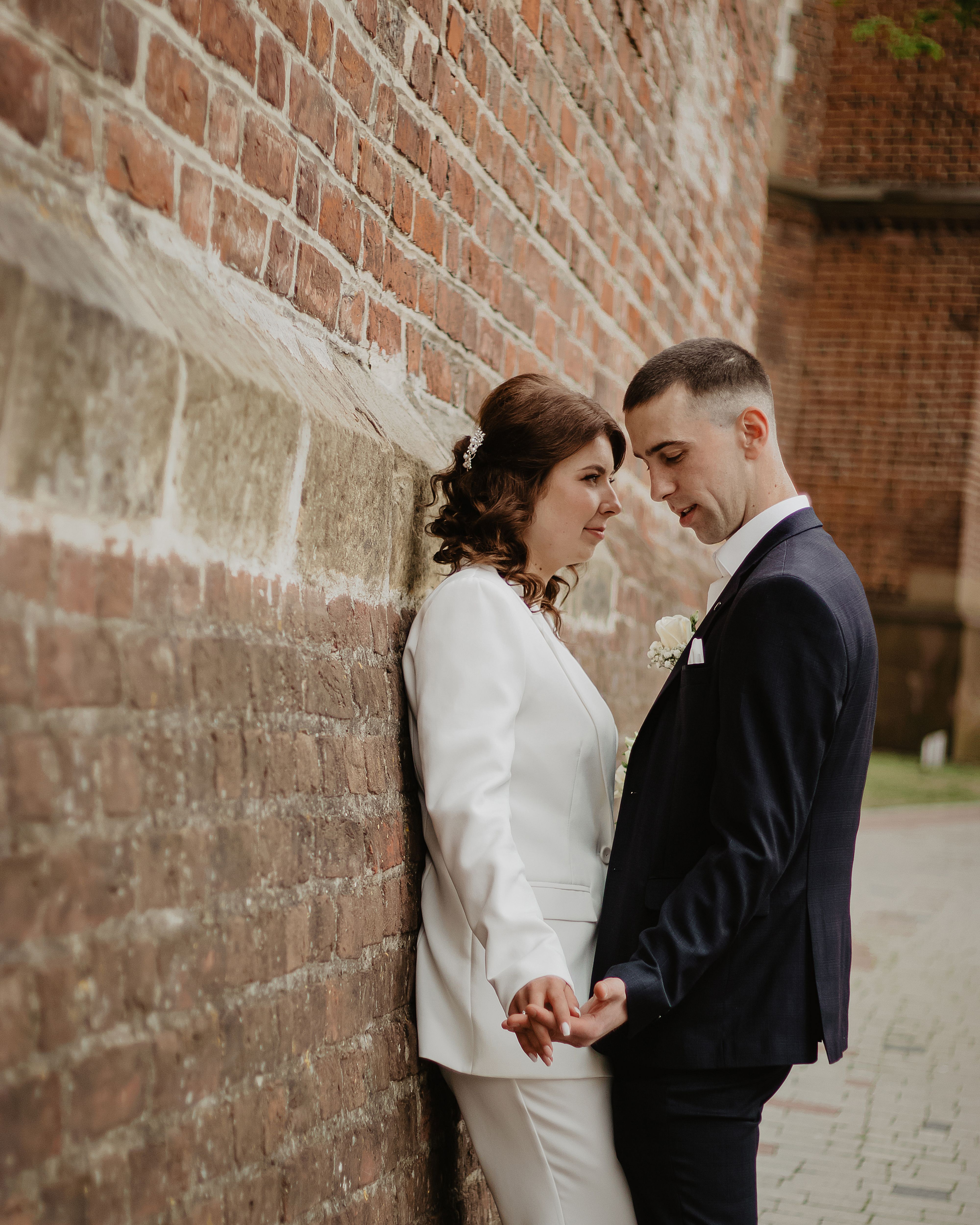 A romantic moment of newlyweds holding hands beside a rustic brick wall outdoors.
