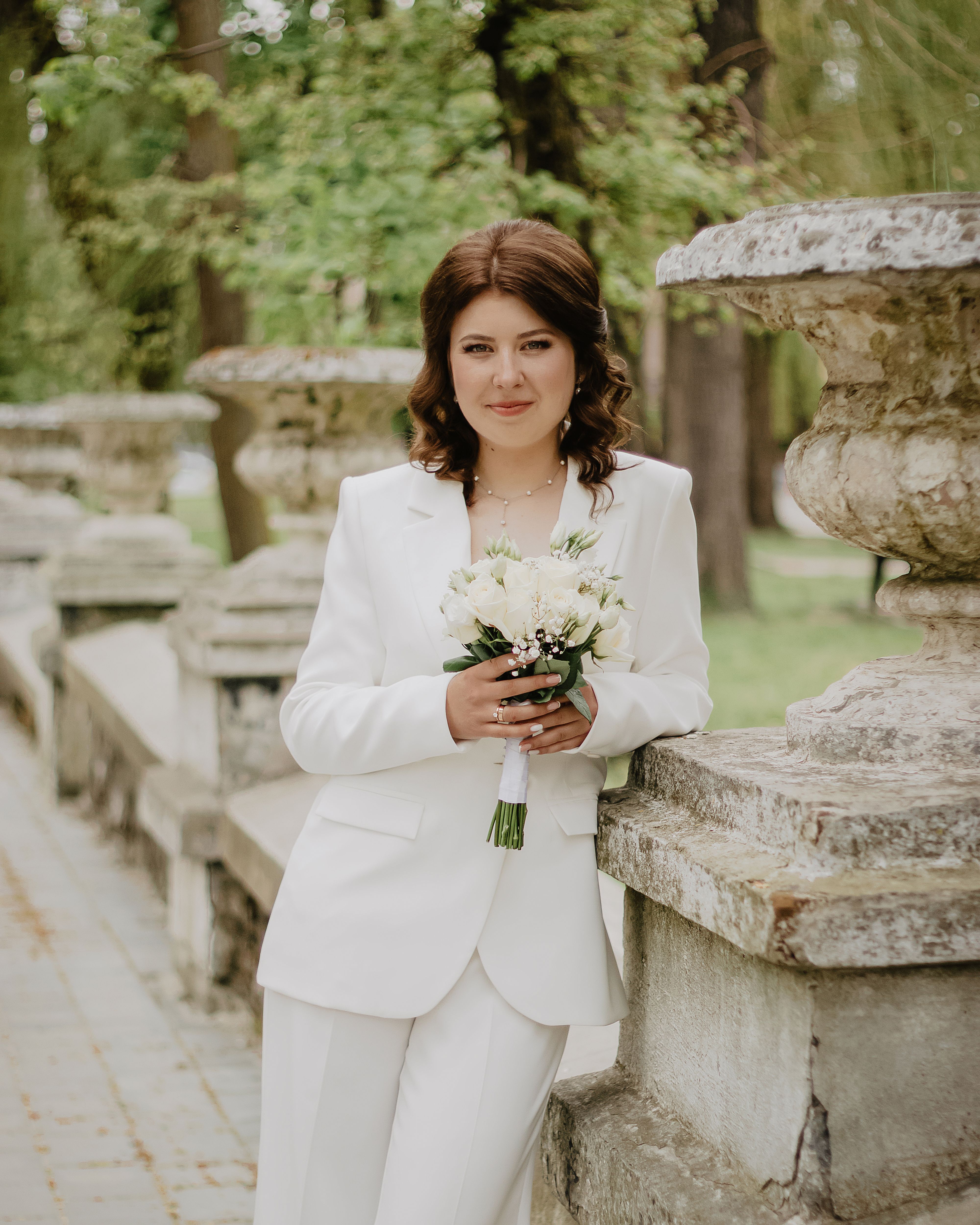 Portrait of a woman in white holding a bouquet outdoors with a serene expression.