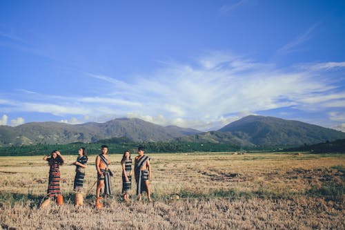Five People Wearing Native Apparel Standing on Brown Grassfield Under Blue and White Cloudy Sky