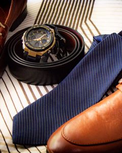 Close-up of elegant leather shoes, wristwatch, belt, and tie on striped fabric. Perfect for men's fashion.