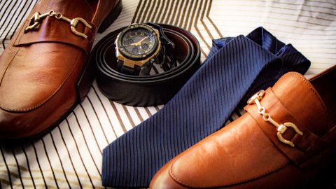 Close-up of elegant leather shoes, wristwatch, belt, and tie on striped fabric. Perfect for men's fashion.