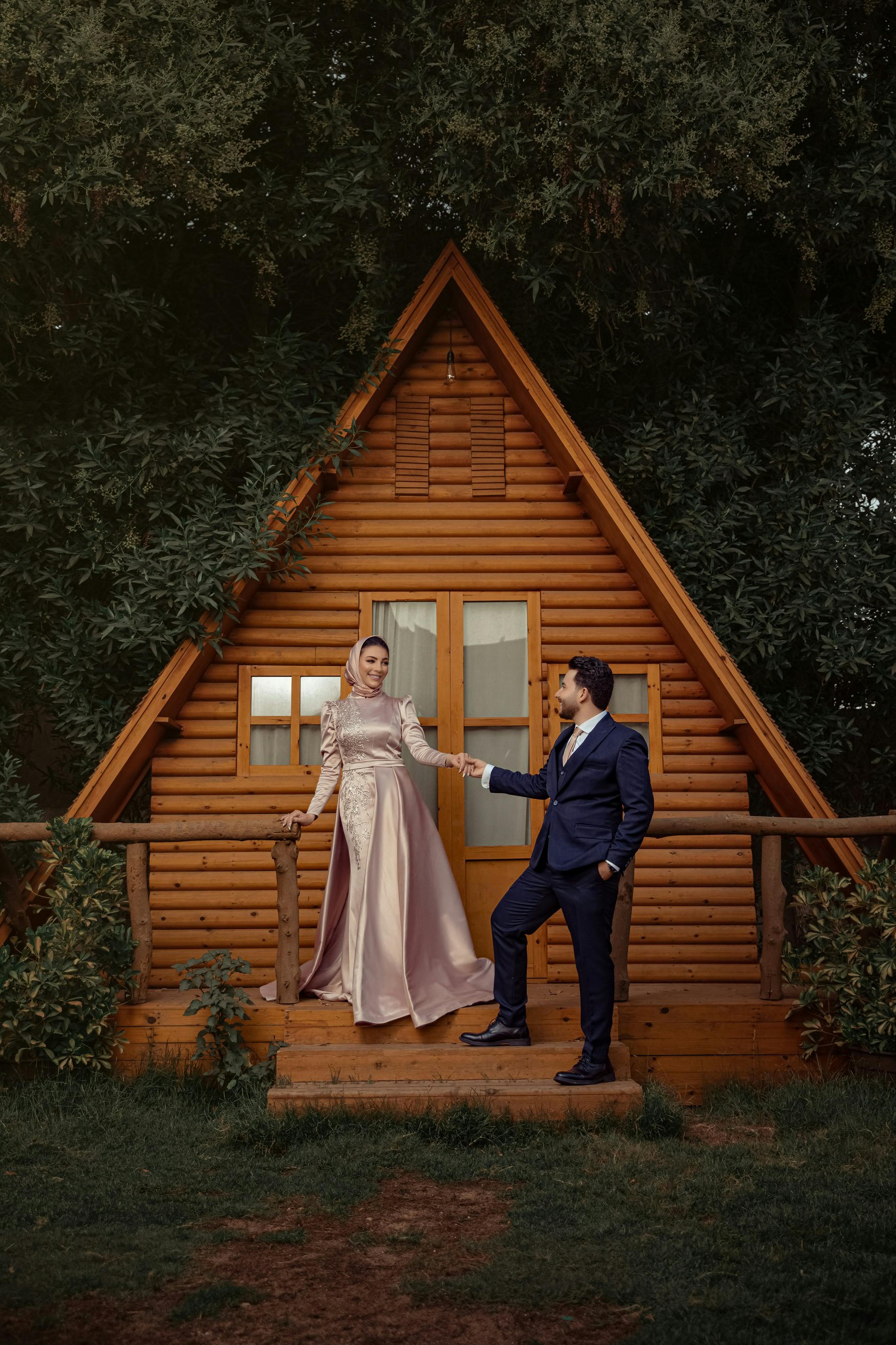 Couple in traditional attire posing romantically in front of a rustic wooden cabin.