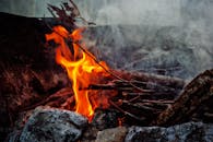 特写镜头中，营火舞动，烟雾缭绕，四周环绕着原木和石头