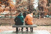 两个朋友坐在萨拉热窝秋天公园的长凳上，周围是秋叶