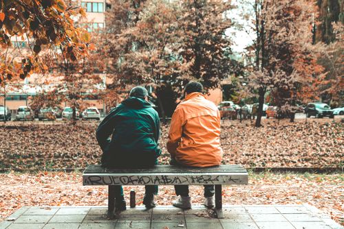 Free Two friends sit on a bench in an autumn Sarajevo park surrounded by fall foliage. Stock Photo
