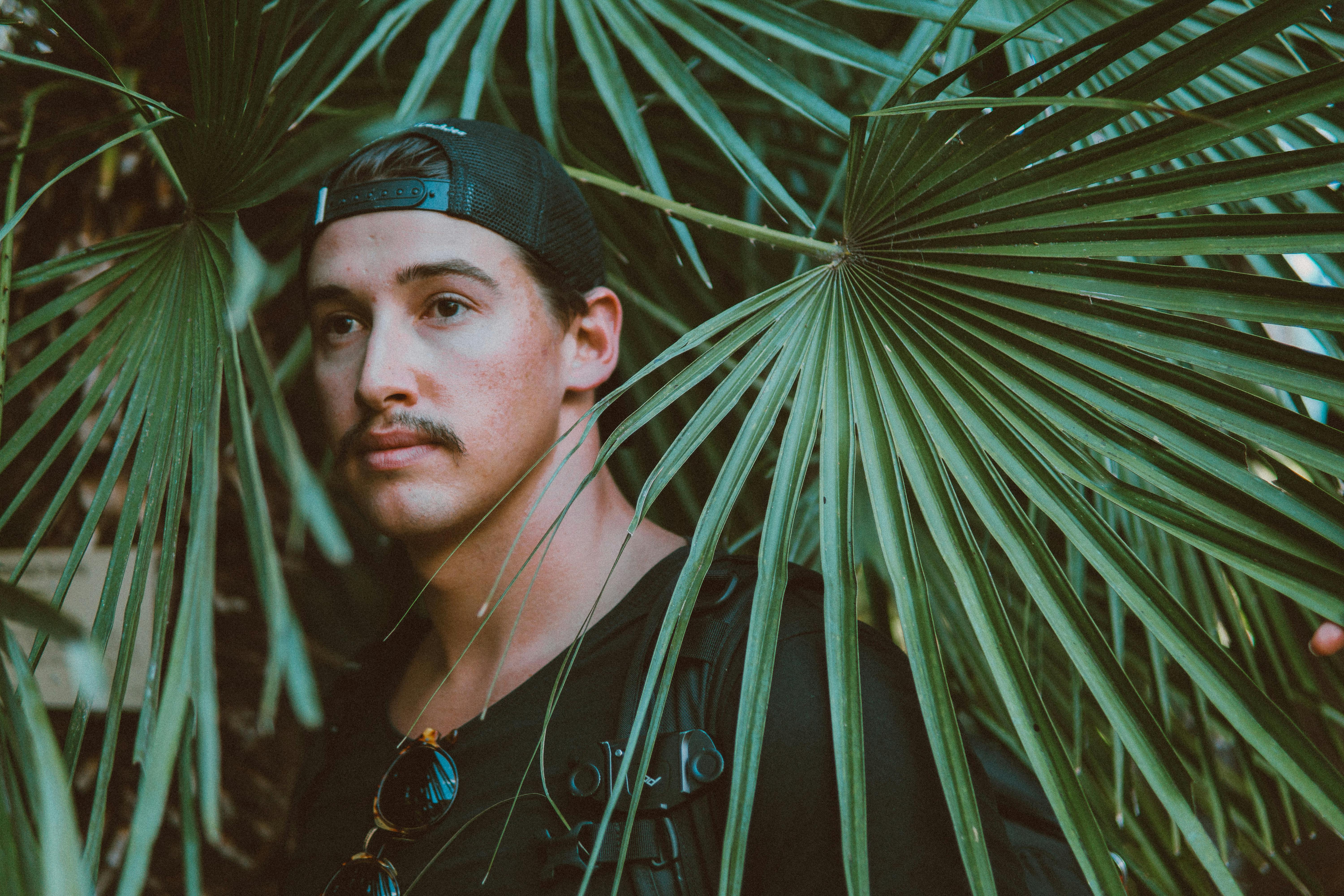 一名男子戴着帽子和太阳镜，生活在绿叶繁茂的热带环境中