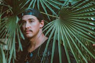 一名男子戴着帽子和太阳镜，生活在绿叶繁茂的热带环境中