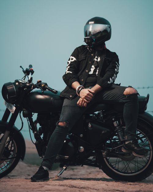 Free A motorcyclist in trendy attire sits confidently on a sleek black motorcycle in an outdoor setting. Stock Photo