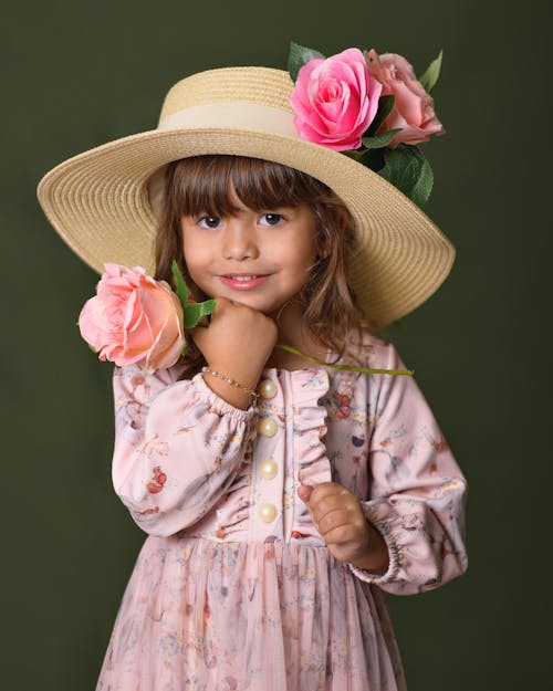 Studio Shot of a Little Girl in a Dress and Hat and Holding a Rose 