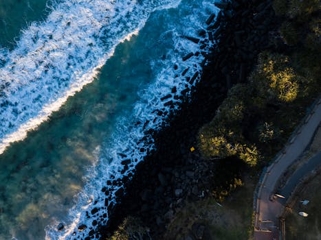 A stunning aerial view capturing the ocean waves crashing against a rocky shore with scenic landscape.