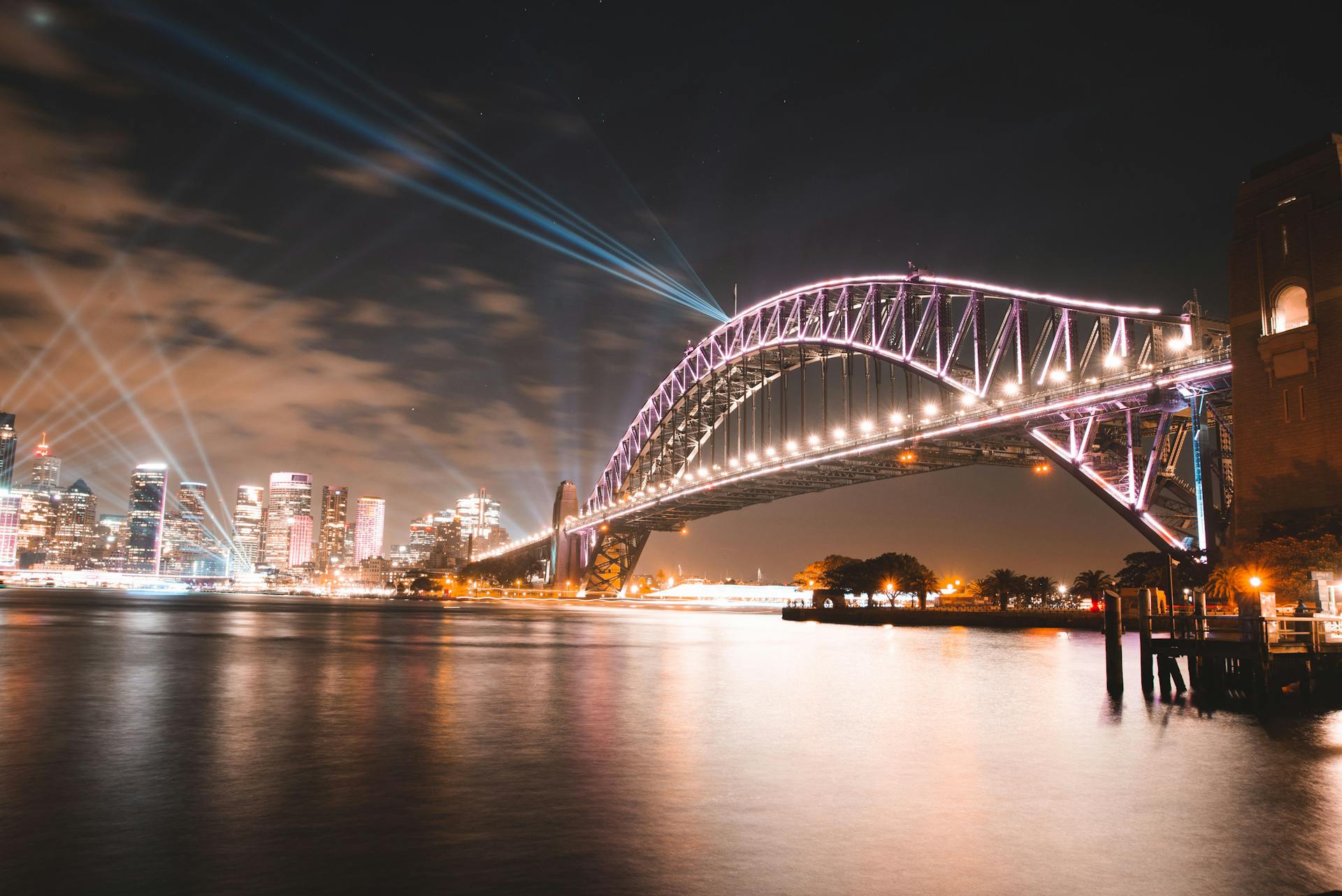 Stunning view of illuminated Sydney Harbour Bridge with city skyline and reflections over water at night.