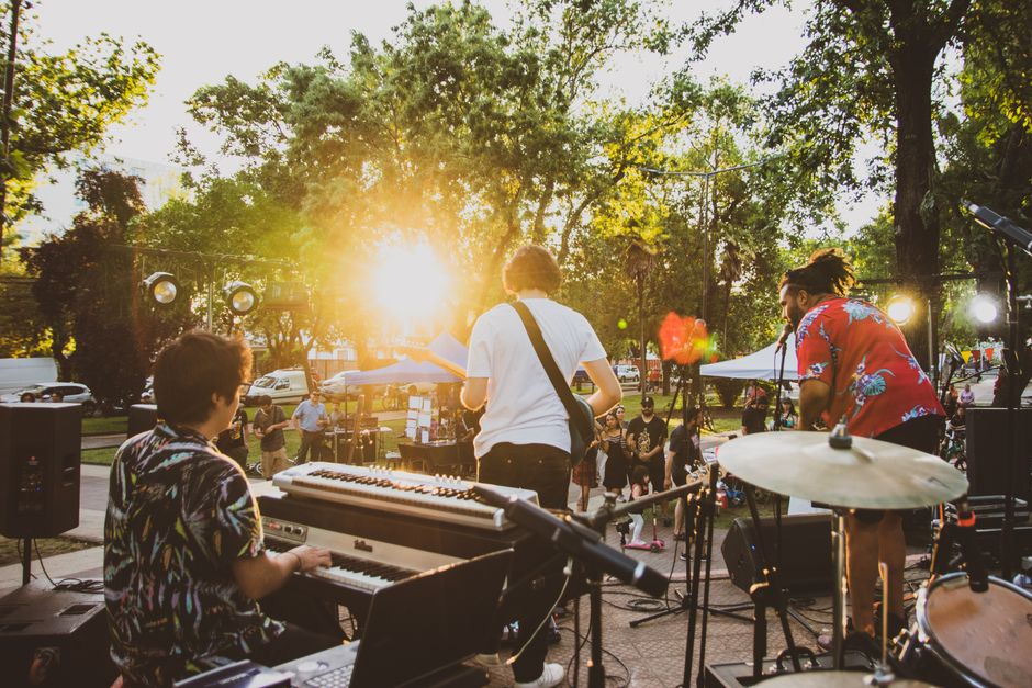 Musicians performing live at a summer outdoor concert during sunset in a park.
