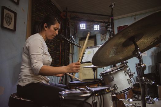 Female drummer practicing in a home studio setup with microphone and drum kit.