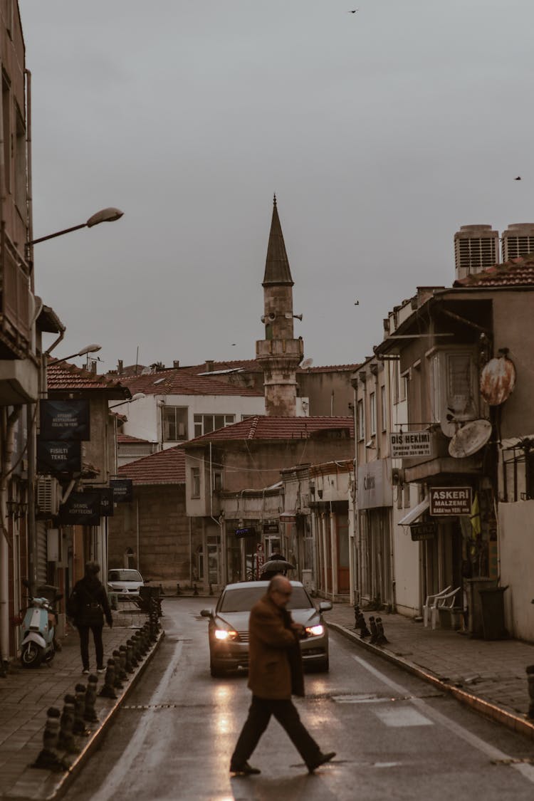 Man Crossing Street With Minaret Behind Buildings