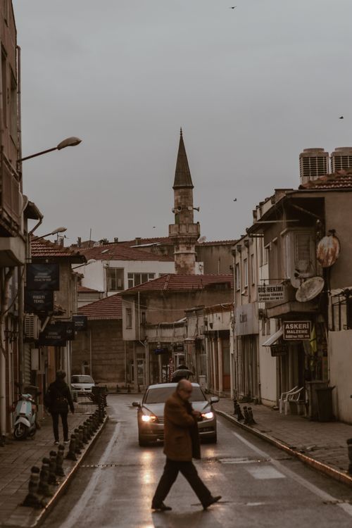 Free Man crossing a rainy street in a historical town with a minaret in the background. Stock Photo