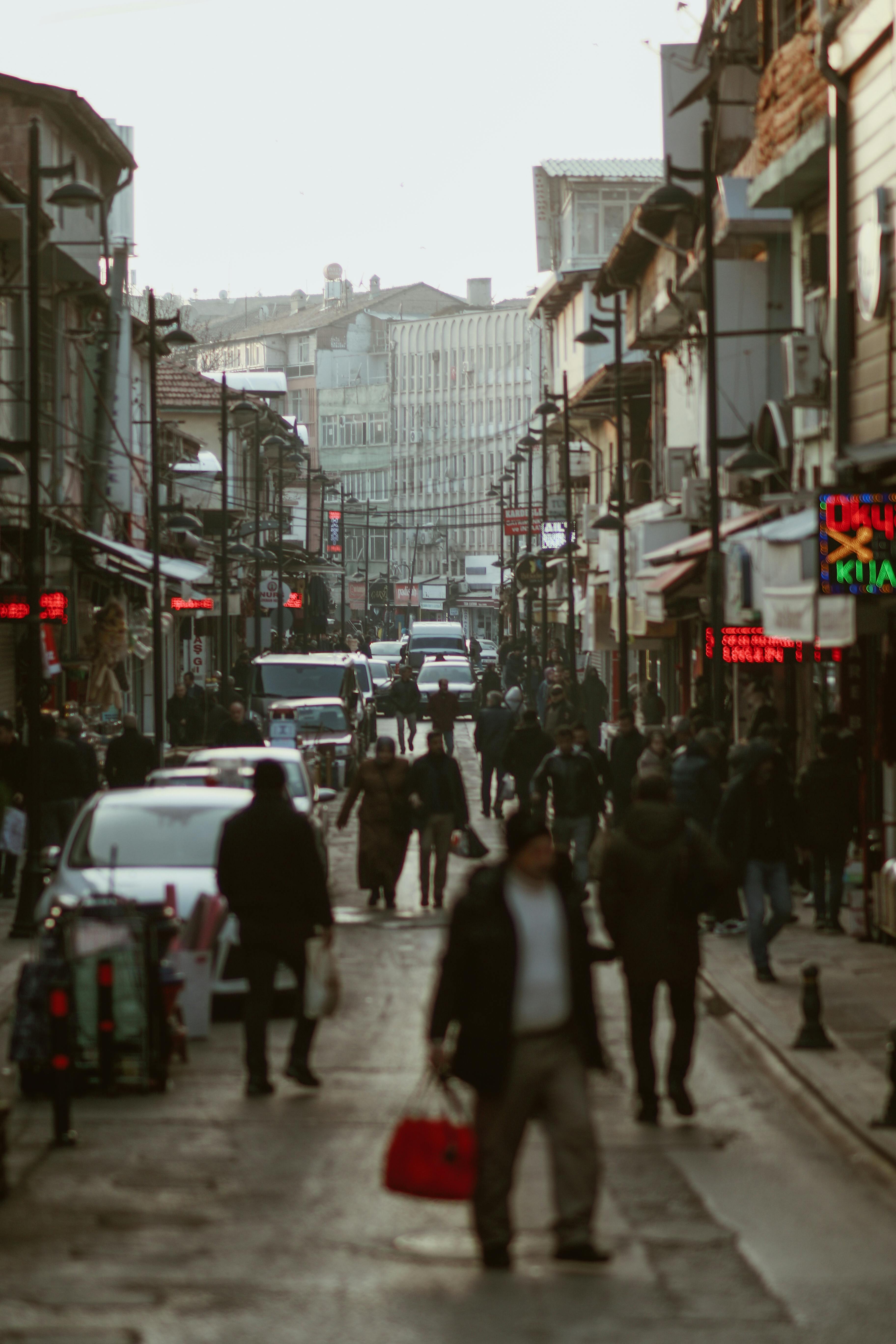 Crowded urban street scene with people walking, cars passing, and vibrant city life.