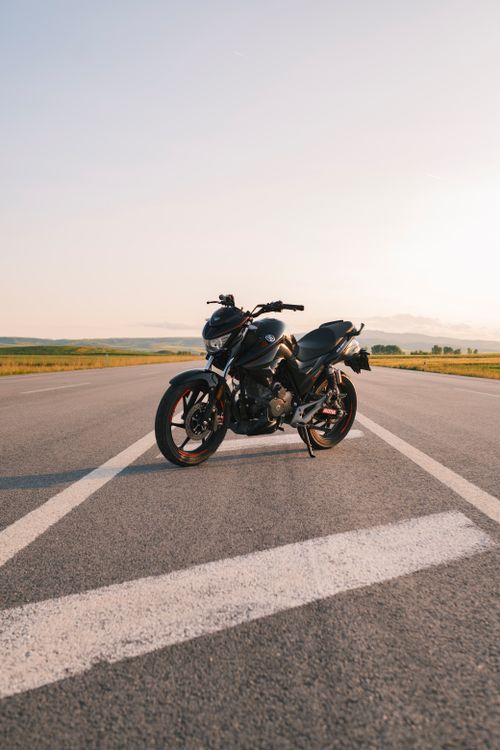 Free A motorcycle parked on a deserted road during daylight, under a clear sky. Stock Photo