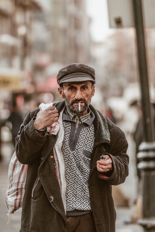 Free Candid street photo of an elderly man wearing a cap, smoking and walking in the city. Stock Photo
