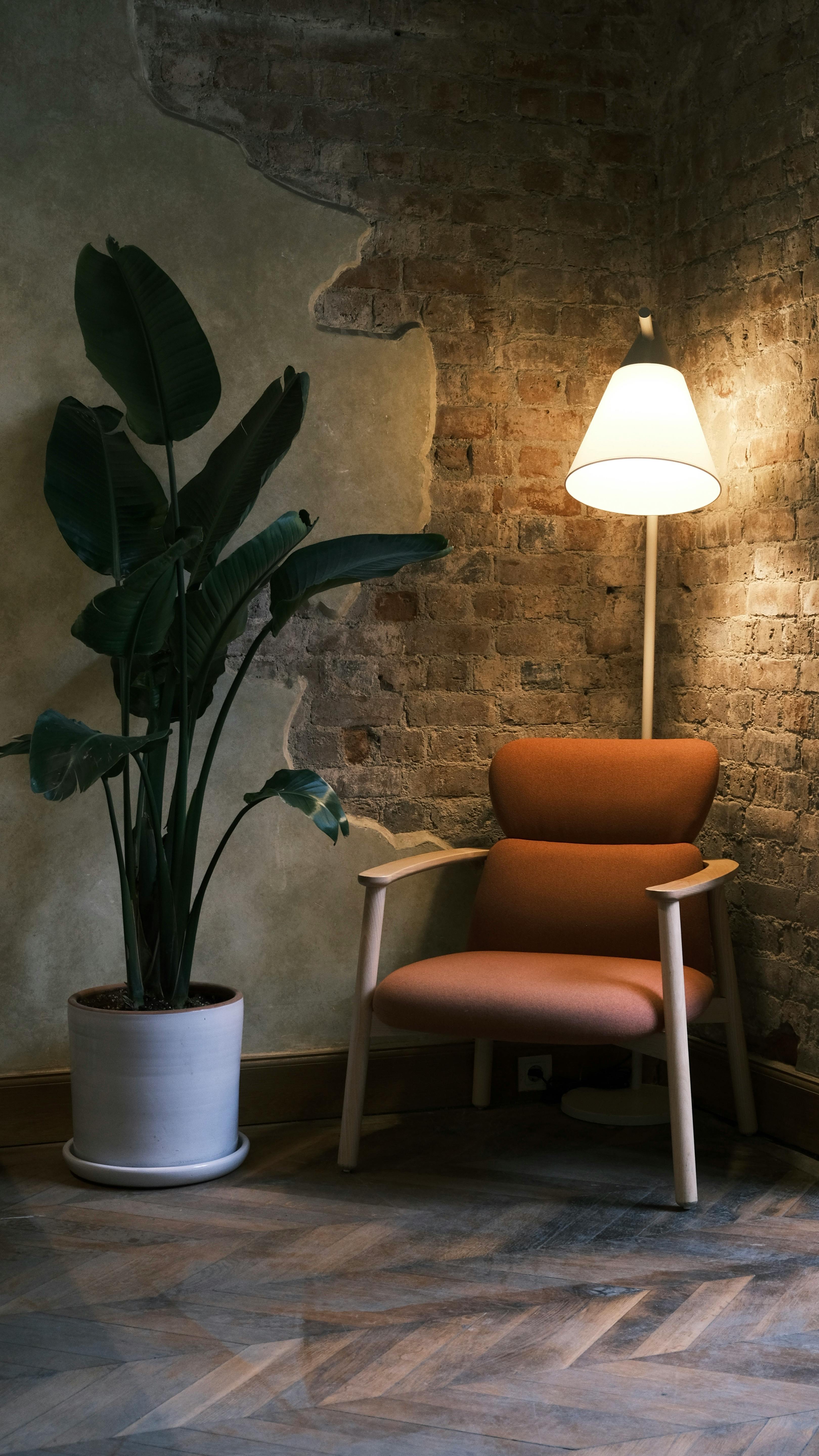 Free A cozy corner with a modern armchair, floor lamp, and houseplant against brick walls. Stock Photo