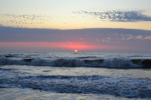 Free A beautiful sunset over the ocean with rolling waves and a cloud-streaked sky. Stock Photo