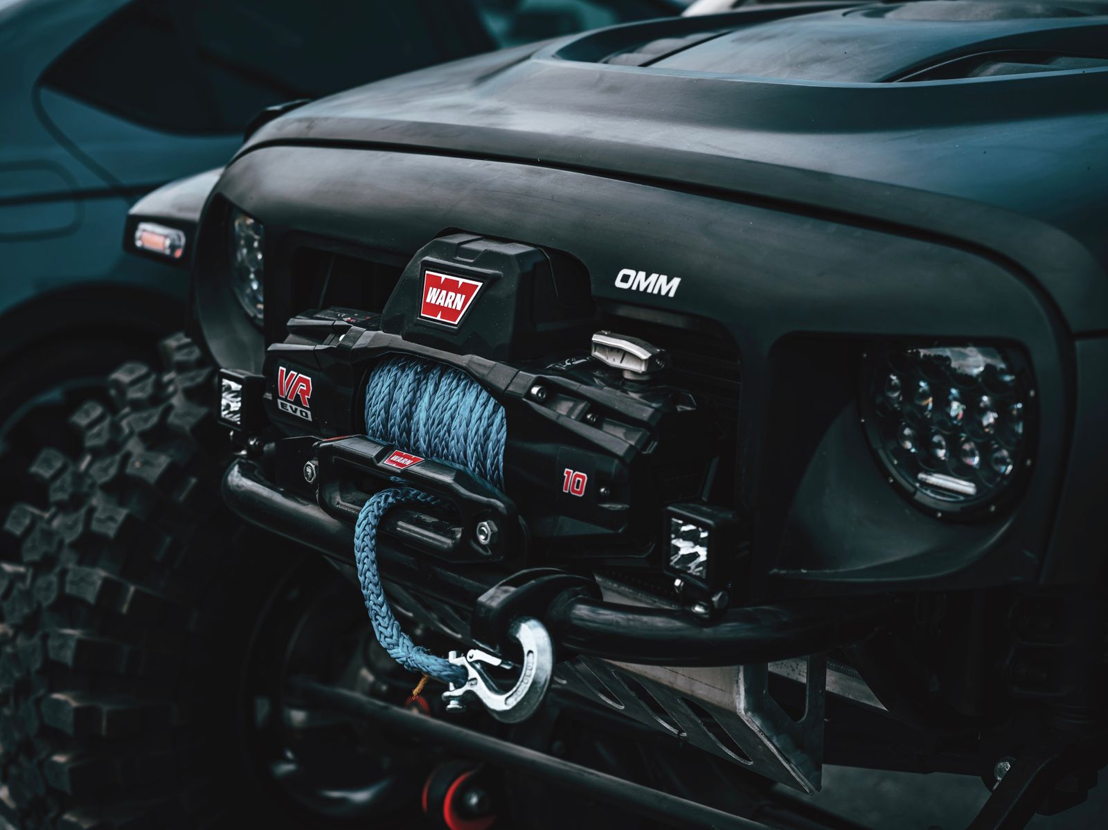 Modern off-road winch loaded with blue synthetic rope mounted on a matte-black 4x4 front bumper