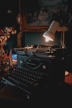 Classic Mercedes typewriter under lamp on antique desk, cozy vintage ambiance.