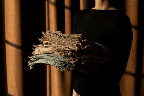 Free A woman holds folded fabric with textured lines in artistic shadows indoors. Stock Photo