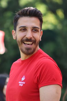 A cheerful adult male with short black hair and a red t-shirt smiling outdoors. - Fotografer Sidoarjo