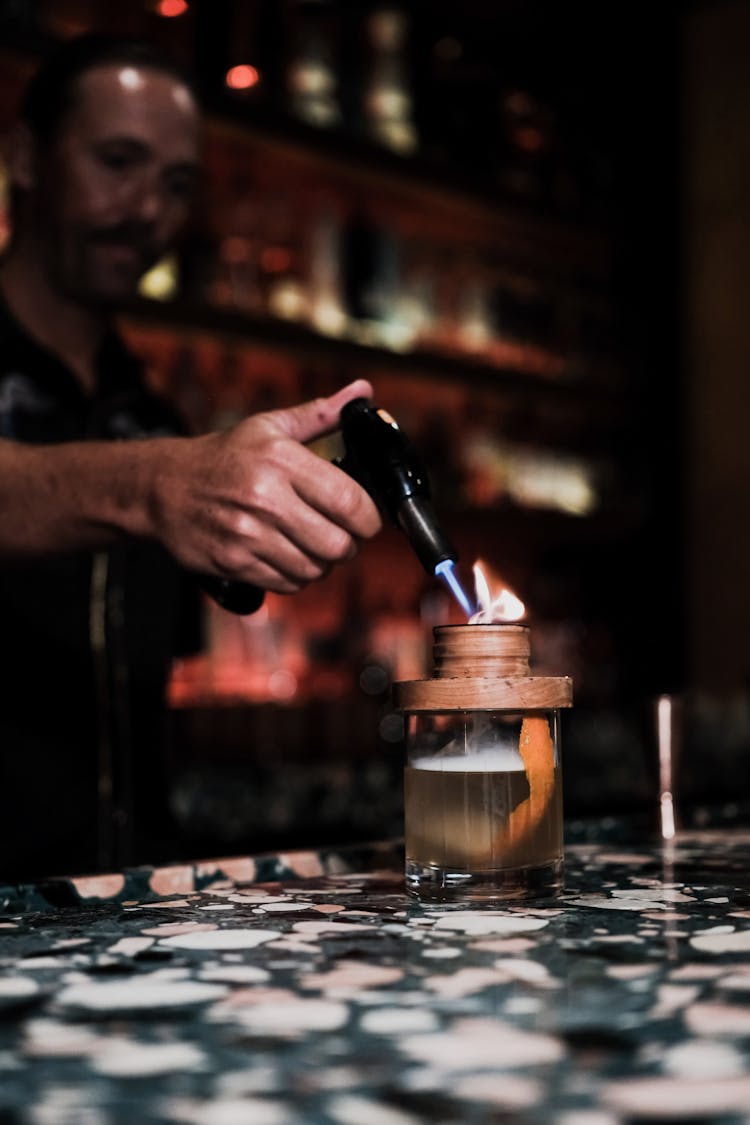 Bartender With Burner Making Cocktail At Bar