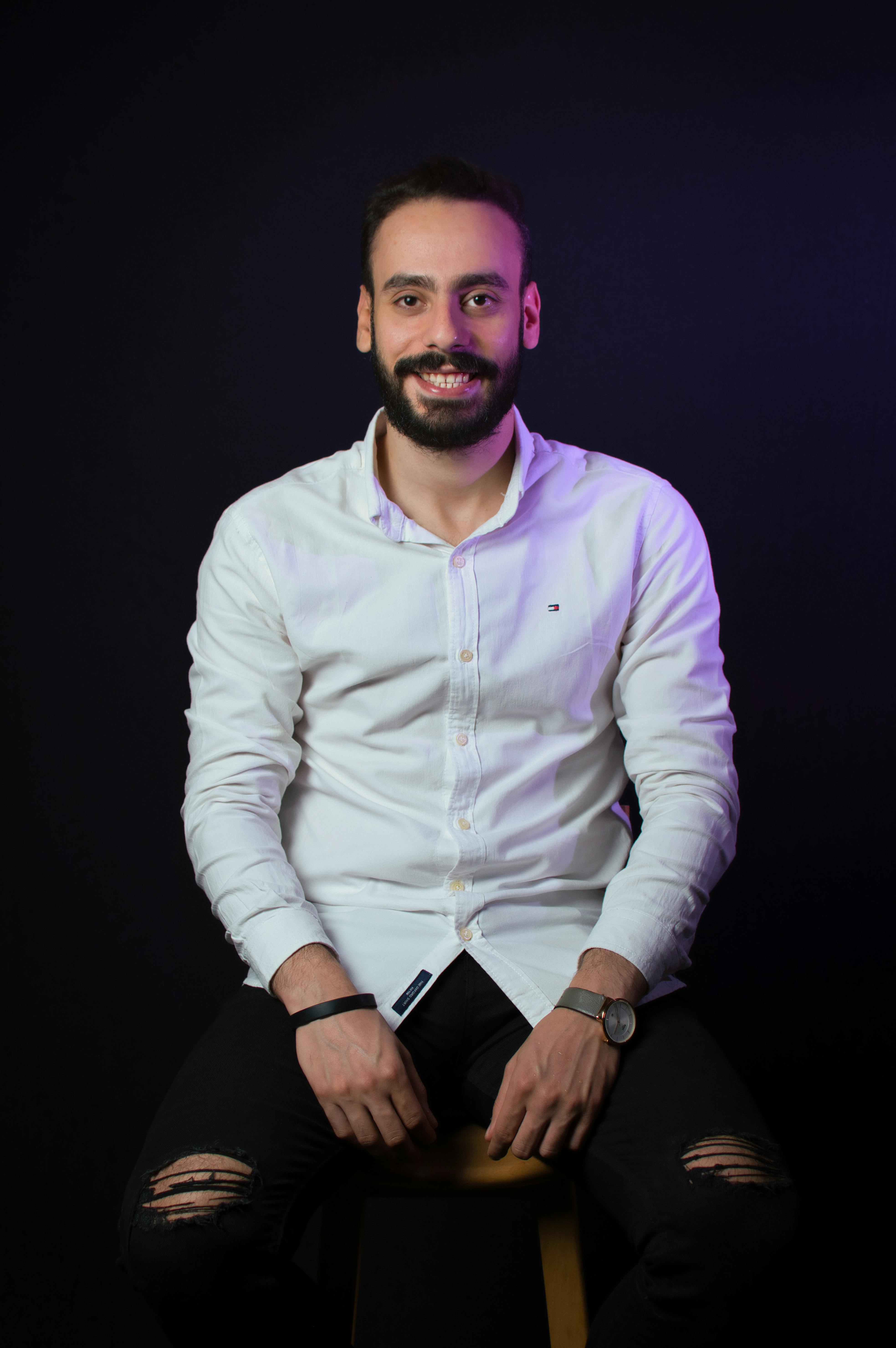 Studio portrait of a smiling young bearded man in a white shirt.
