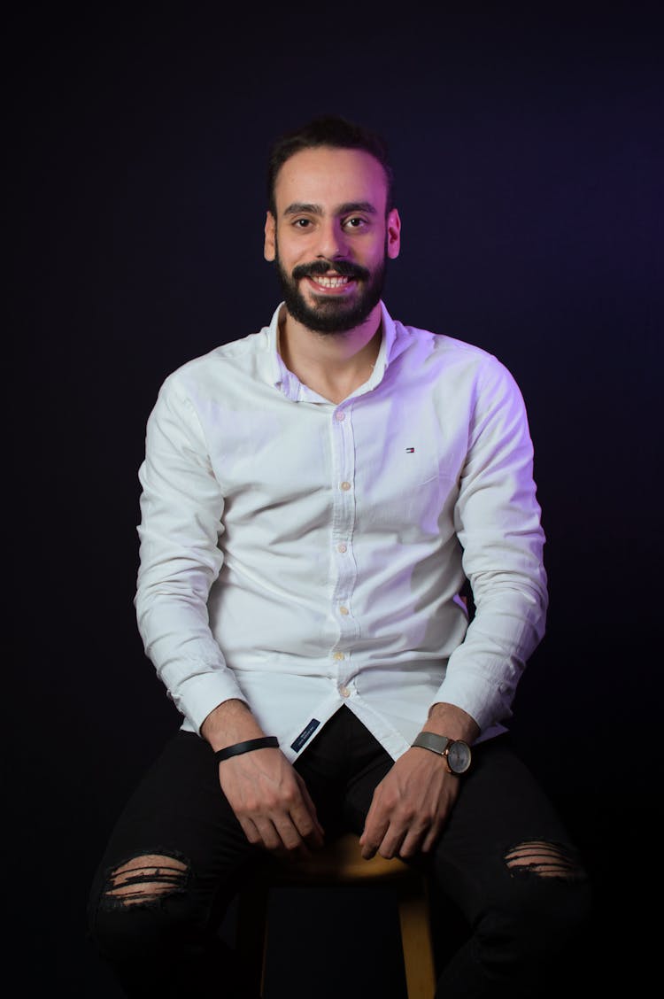 Portrait Of Smiling Bearded Man Sitting On Stool In Studio