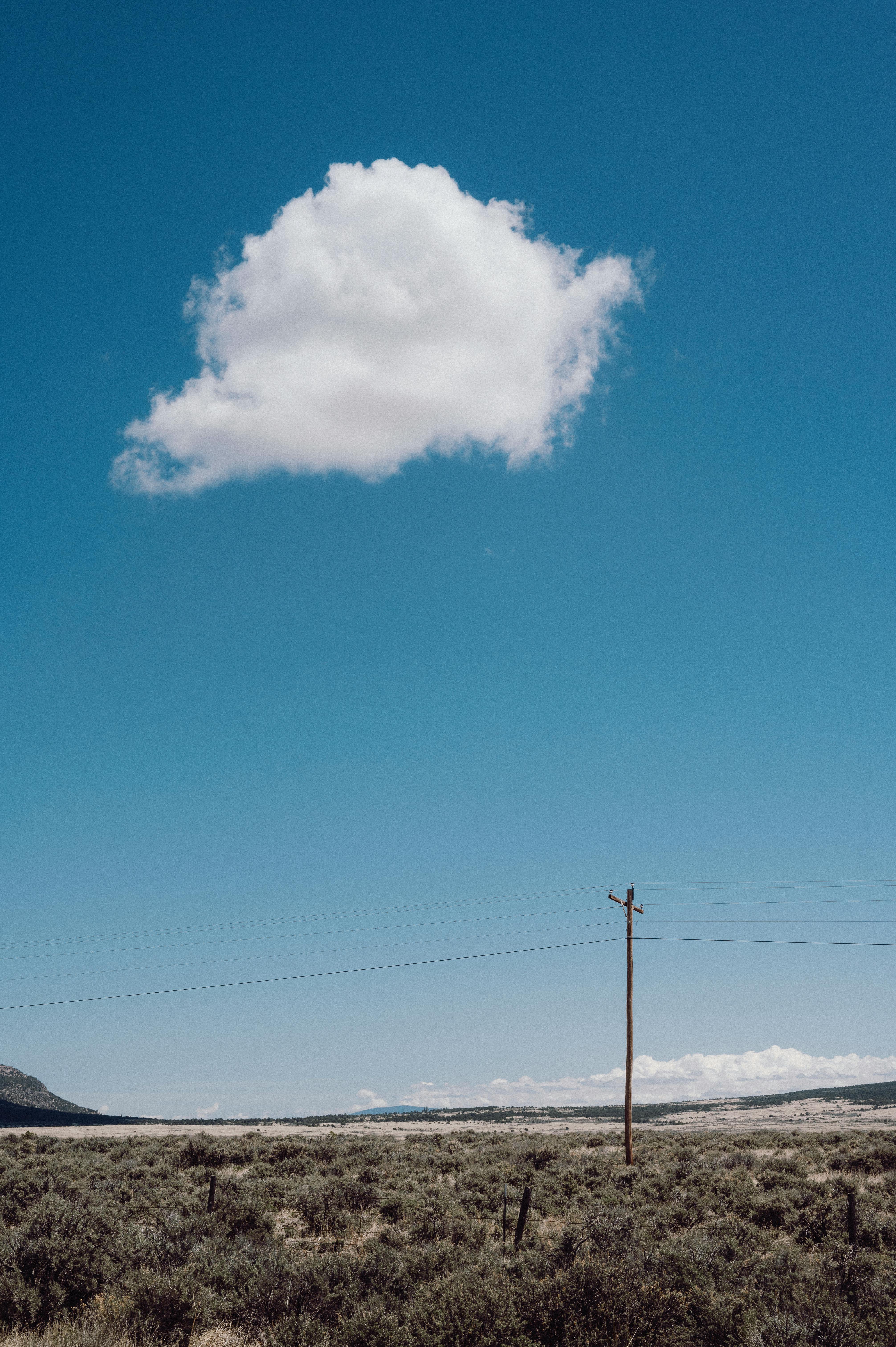 Serene landscape with a single cloud in a vast blue sky over a rural field.