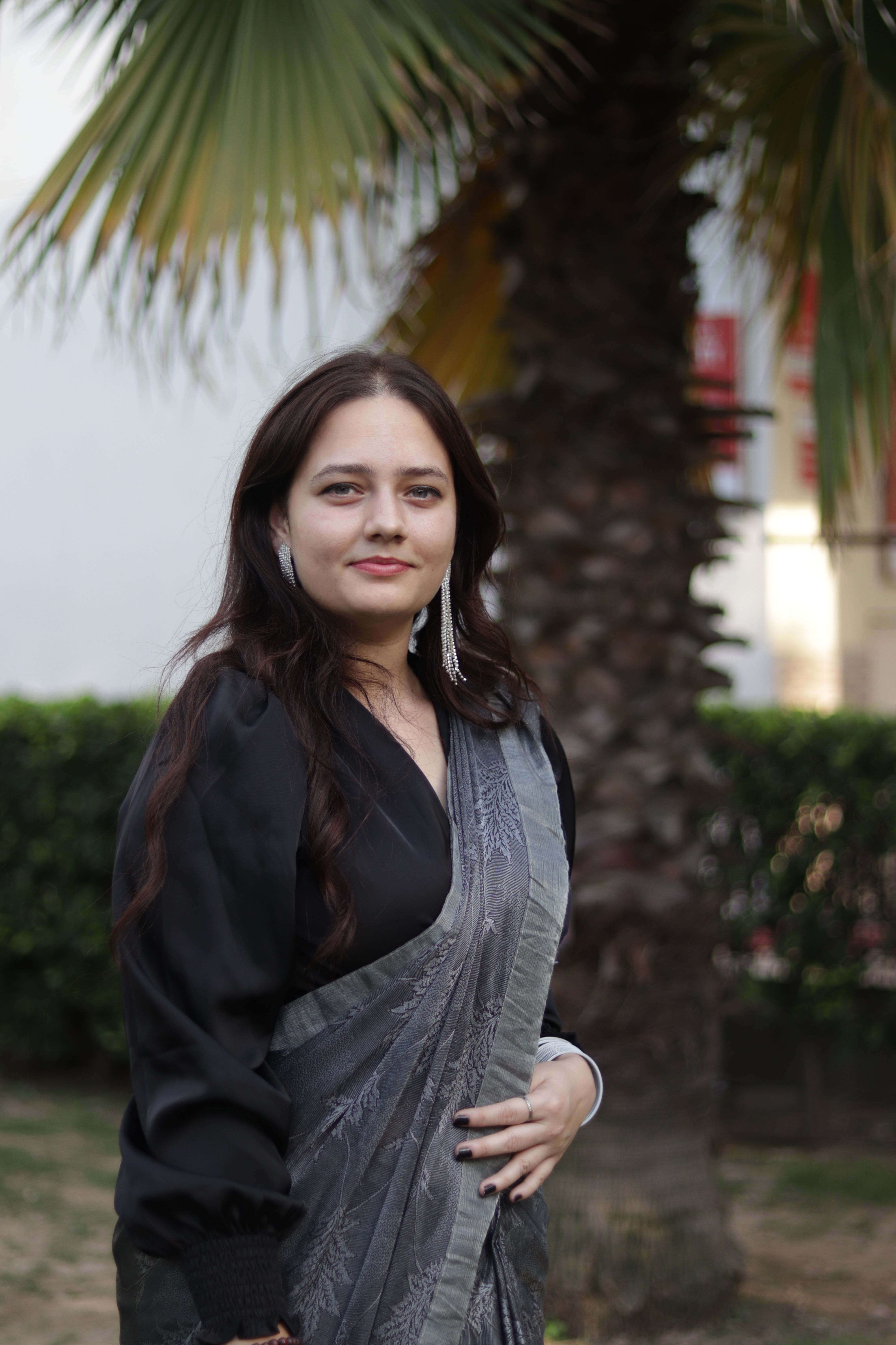 Confident woman wearing a traditional saree, standing elegantly in a garden setting.