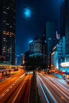 Dynamic urban night scene showcasing skyscrapers and vibrant light trails under a moonlit sky.