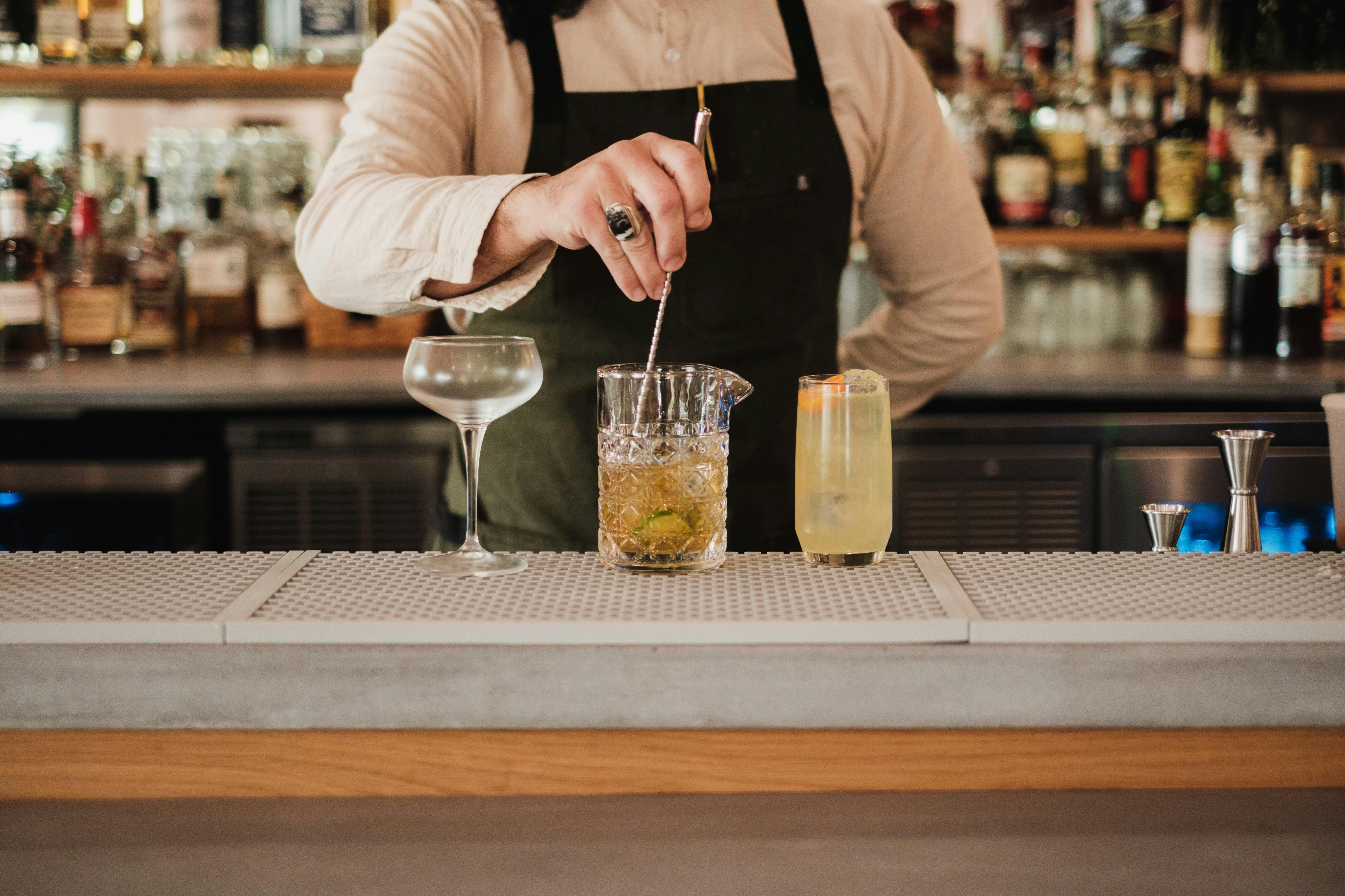 Bartender crafting cocktails at a well-stocked bar, showcasing expert mixology skills.
