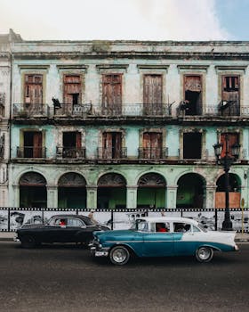Classic cars cruising past a vintage building in Havana, Cuba. Urban nostalgia and retro vibe.