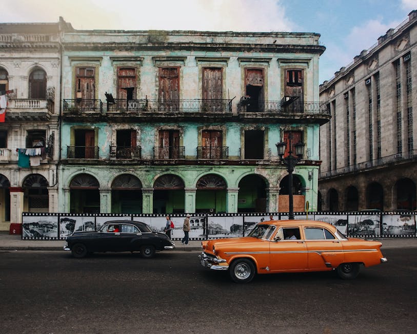 Classic cars passing by a decaying historic building in Havana, Cuba, showcasing vintage urban charm.