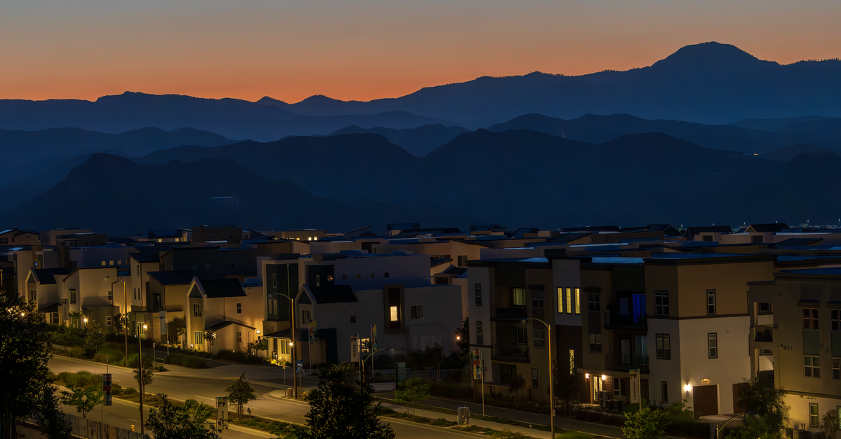 A quiet suburban neighborhood illuminated at dusk with mountains in the background.