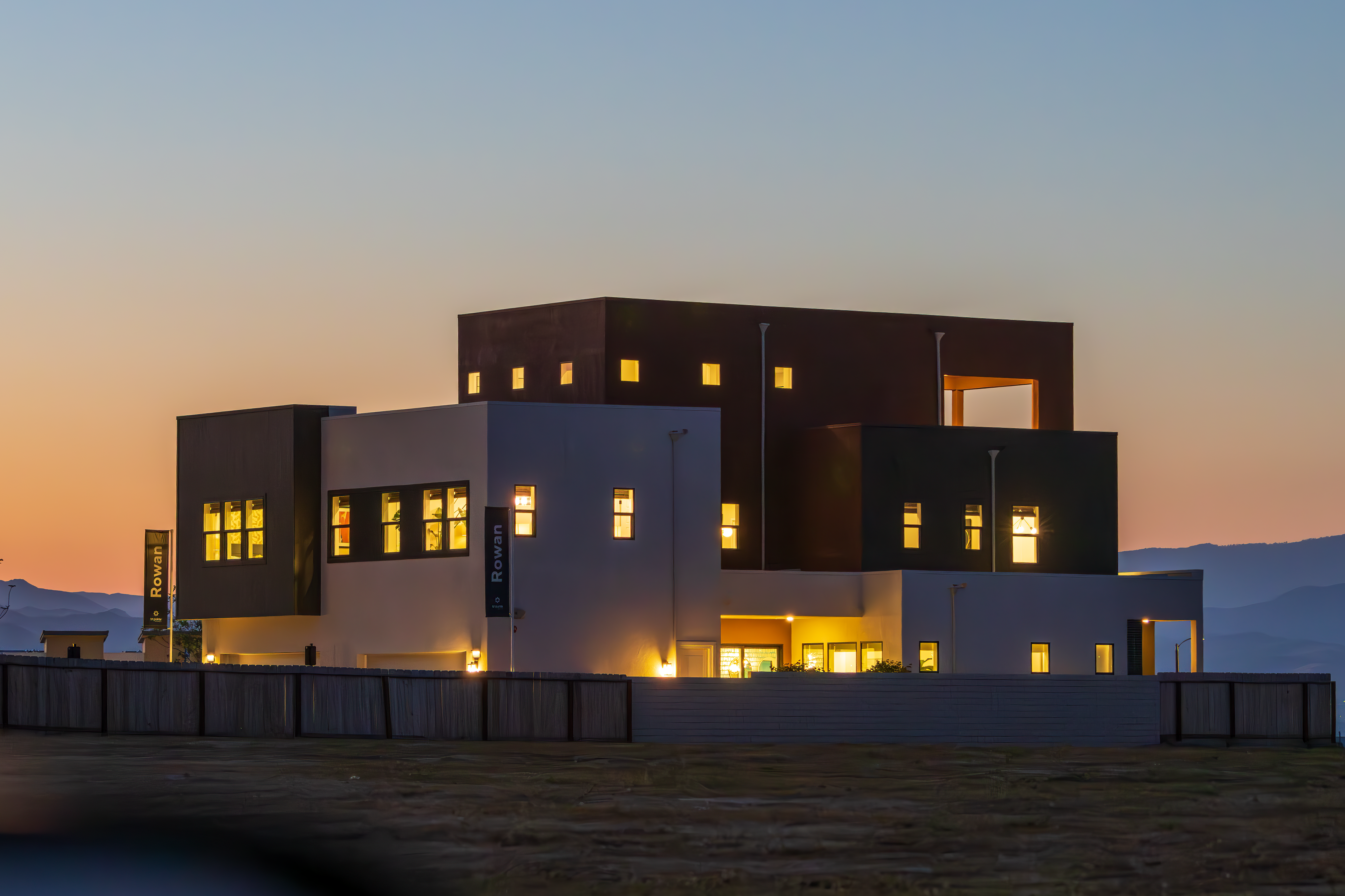 Modern building with lit windows at dusk on a grassy field under a twilight sky