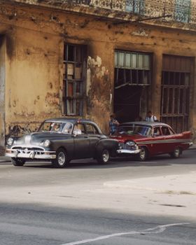 Classic vintage cars parked on a worn city street in Cuba, capturing retro urban decay and travel vibes.