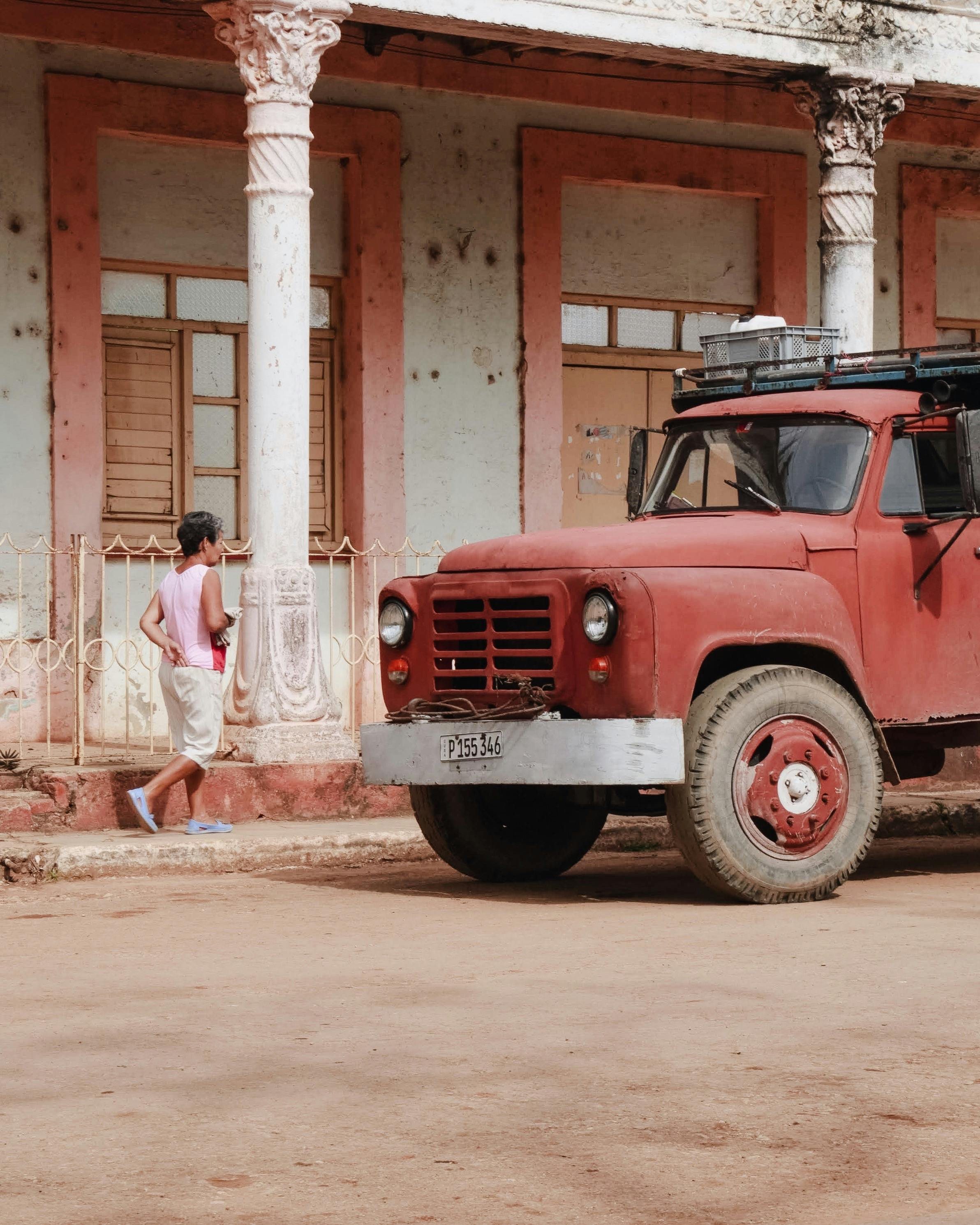 Old red truck parked on rustic urban street with colonial architecture.