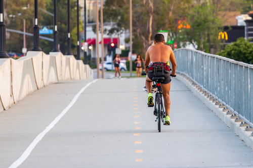 Free A shirtless man riding a bicycle on a city street path during summer. Stock Photo